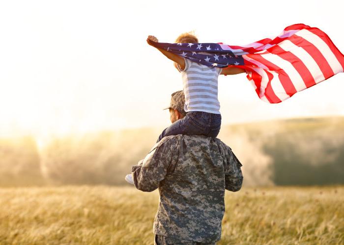 Excited child sitting with american flag on shoulders of father reunited with family